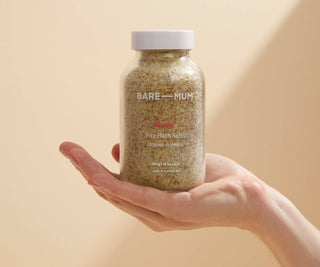 Bare Mum bath salts jar held in a hand against a beige background.