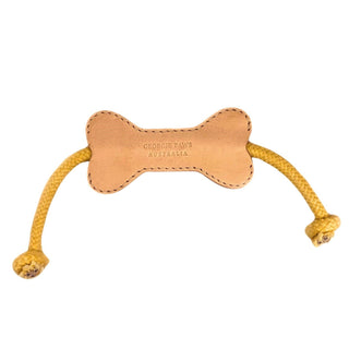 Flora Bone Dog Toy pictured. It is a bone-shaped leather piece that has a cream coloured rope threaded through it. Pictured on a white background.
