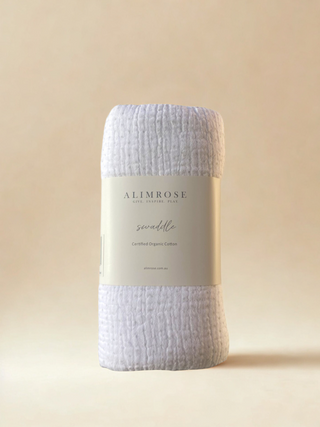 White swaddle with grey spots. 'Alimrose' branded card wrapped around it. Pictured standing up against a beige background.