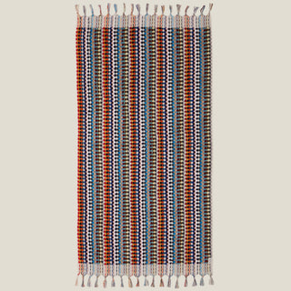 Colourful pom-pom patterned towel with fringe/tassels on a beige background.
